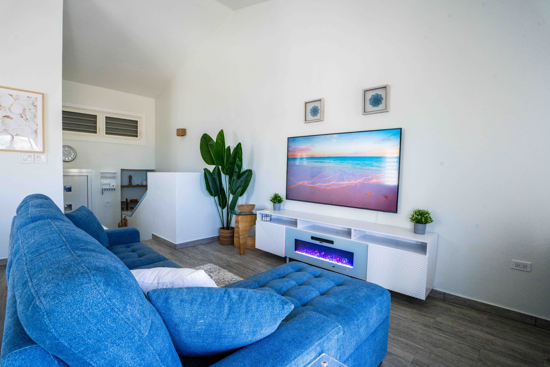 Bright living room with blue sectional, faux fireplace and TV